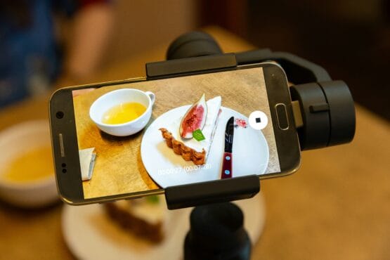 A smartphone mounted on a stabilizer captures a clean, well-lit photo of a plated dish and tea, illustrating how to get better photos of your business using a cell phone and simple tools and techniques.