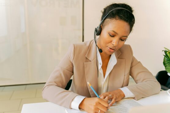 Professional woman wearing a headset and writing notes during a call, representing the personalized support available through free Office Hours with digital marketing specialists.
