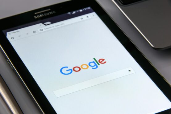 A Samsung tablet displays the Google search homepage, showing the search bar and logo, next to a partial view of a laptop keyboard.