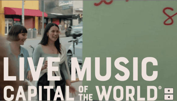 Two women walking on a city sidewalk next to a sign that reads “Live Music Capital of the World.”